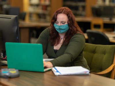 Student looking at a laptop with notes beside her