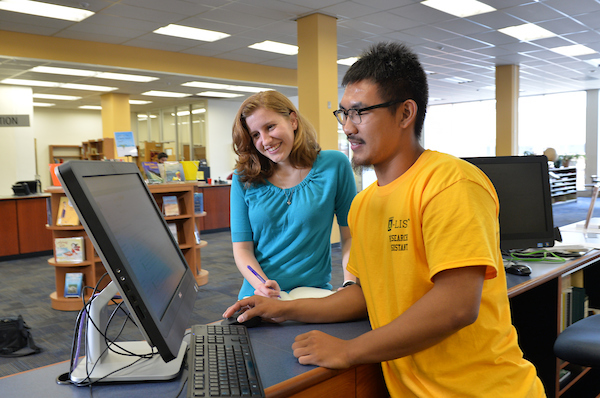 A library employee assists a student with research help